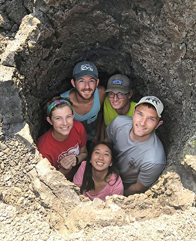 Students standing in hole looking up smiling.