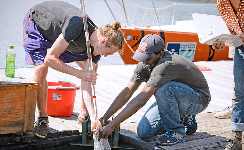 Students at pier performing water tests as another looks on.