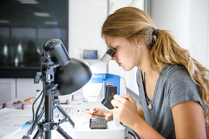 Female student at microscope with oil and rock samples.