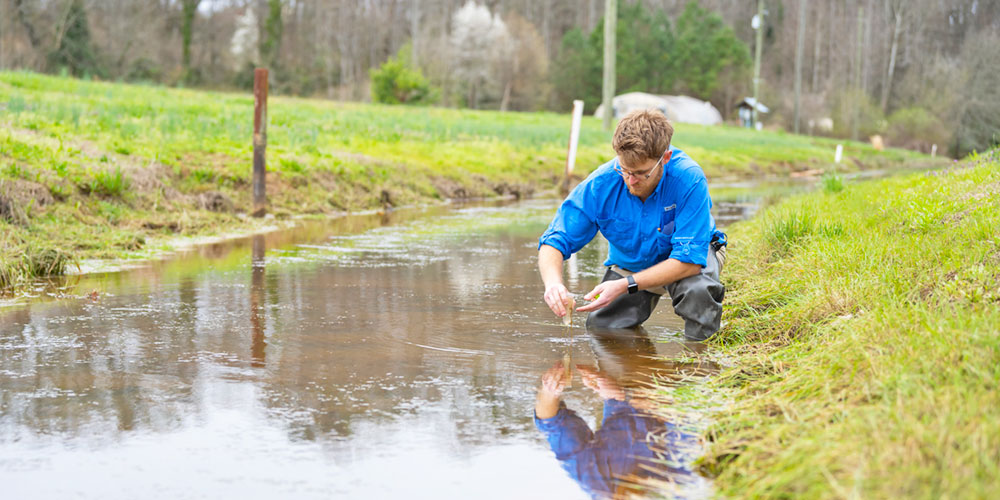 Graduate student performs groundwater testing in small waterway.