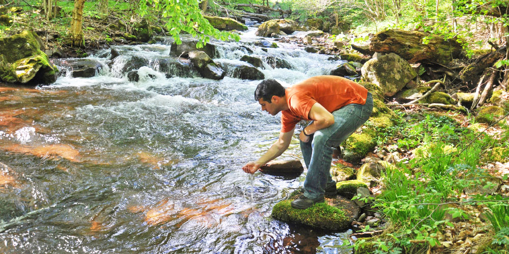 Man leaning over river to test water.