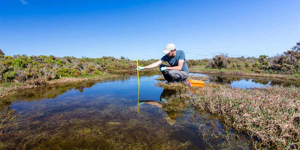 Man using ruler to determine depth of water.