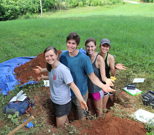 Students in hole with dirt surrounding them.