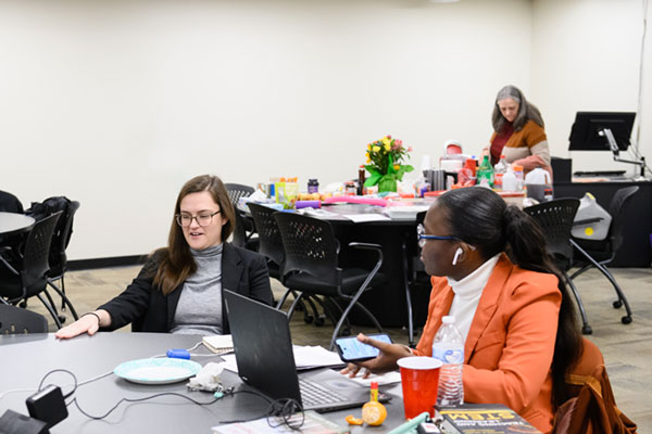 Female students at table with teacher in background