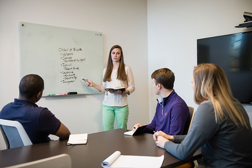 Student at board conversing with other students at table