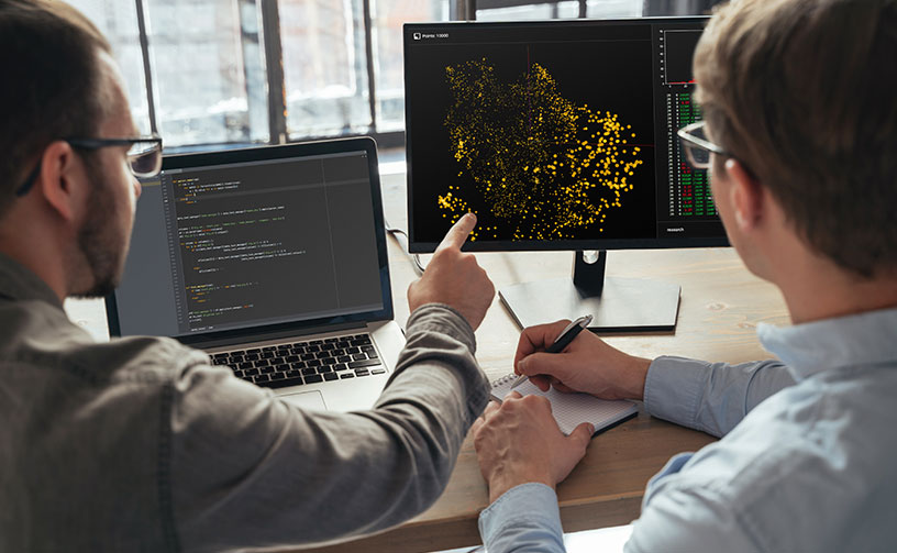 Two people sitting at computer viewing data points.