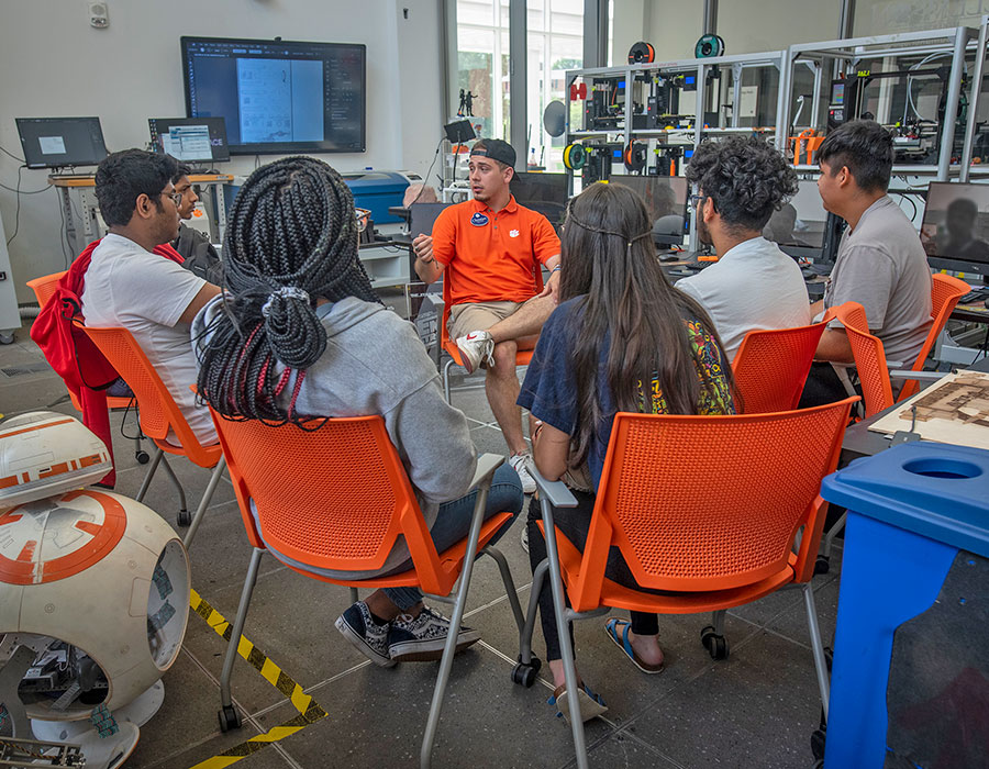 Student in makerspace talking to high schoolers.