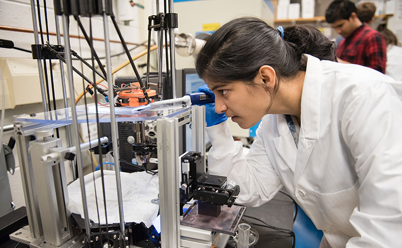 Female student in lab observing equipment.
