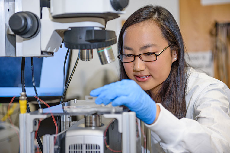 Female in lab examining equipment.