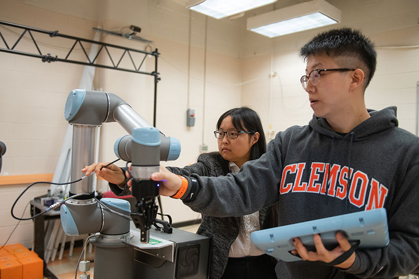 Wang and student in lab with robotic arm.