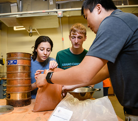 Students and faculty in lab about to mix powder in a bowl.