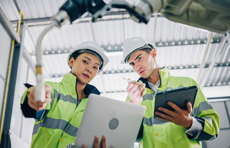 Two employees using laptop to access robotic arm.