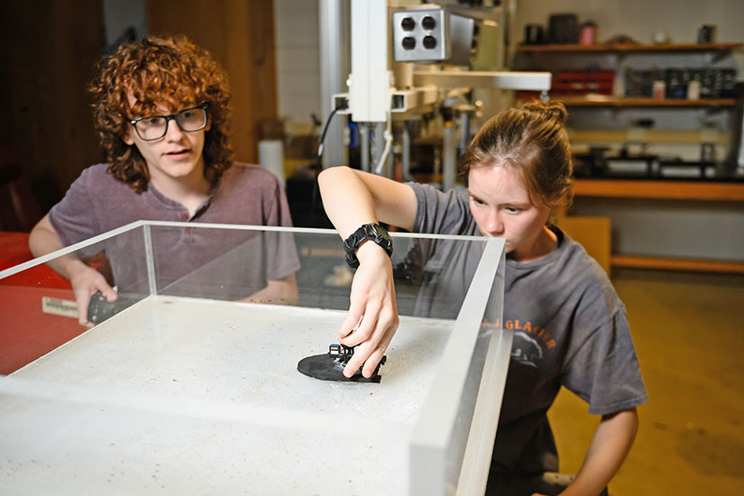 Two students observing motorized mini robotic apparatus.