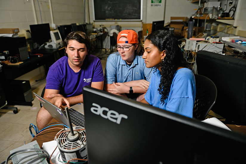 Three students looking at data on a computer and discussing the outcome.