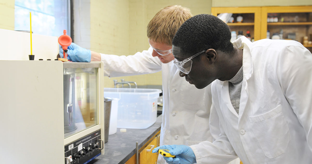 Two students peering into machine in lab