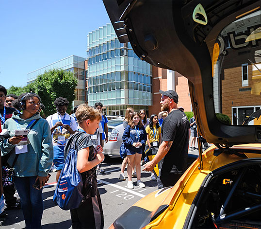 Students outside of Rhodes looking at auto