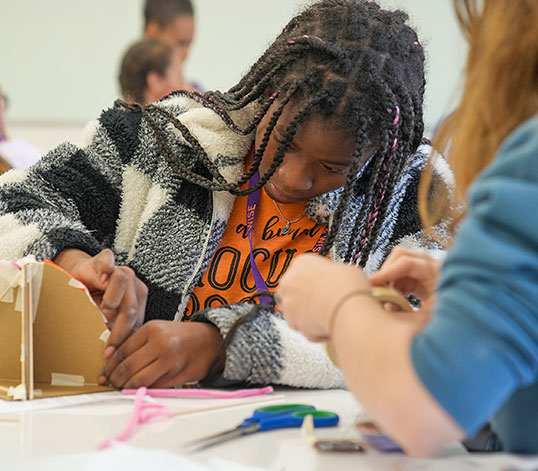 Camp participant building project with help from teacher.