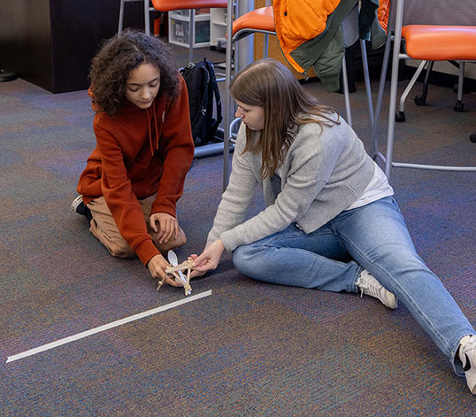 Two participants on the floor helping each other measure item.