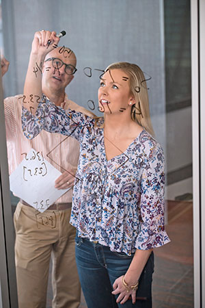 Female student and faculty member using glass wall to solve problem.