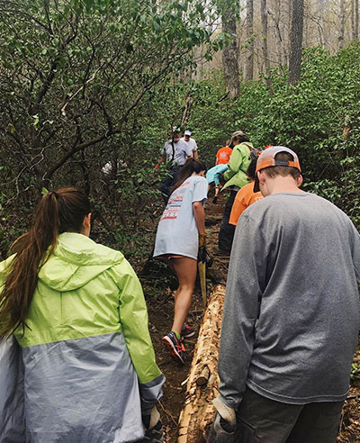 RISE Volunteer Corps in forest carrying logs