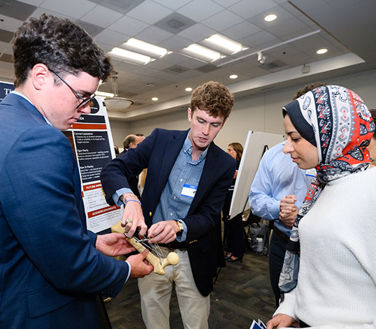 Three students at Bioengineering Symposium looking at neck measurement system.