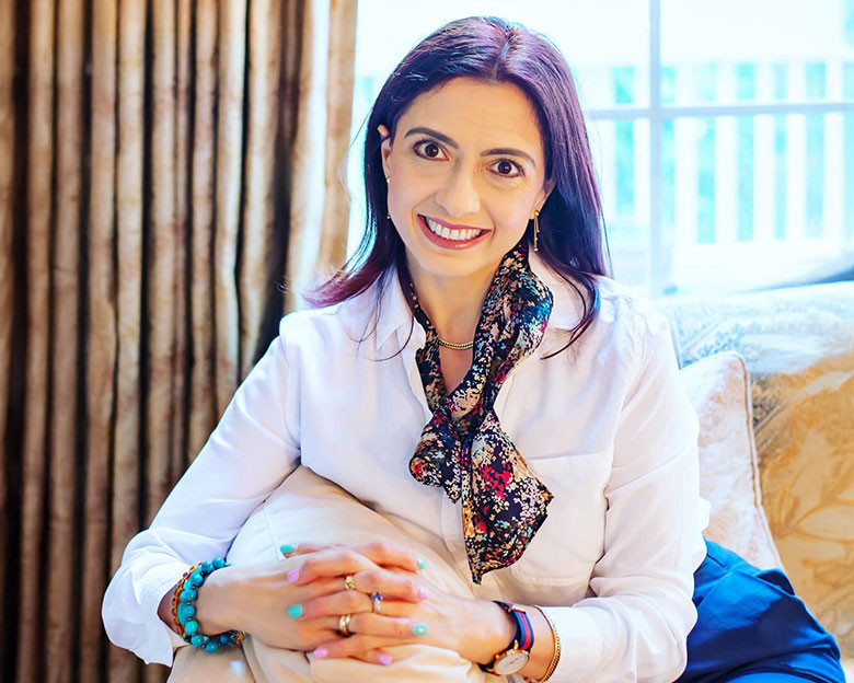 Farnoosh Brock, author, sitting in her living room, smiling at the camera.