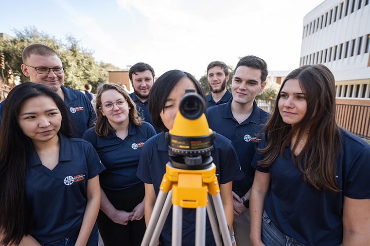 Group with surveying equipment outside of Riggs Hall