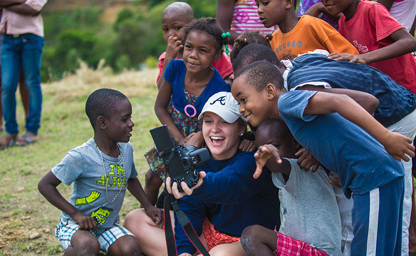 Student intern surrounded by children from Haiti