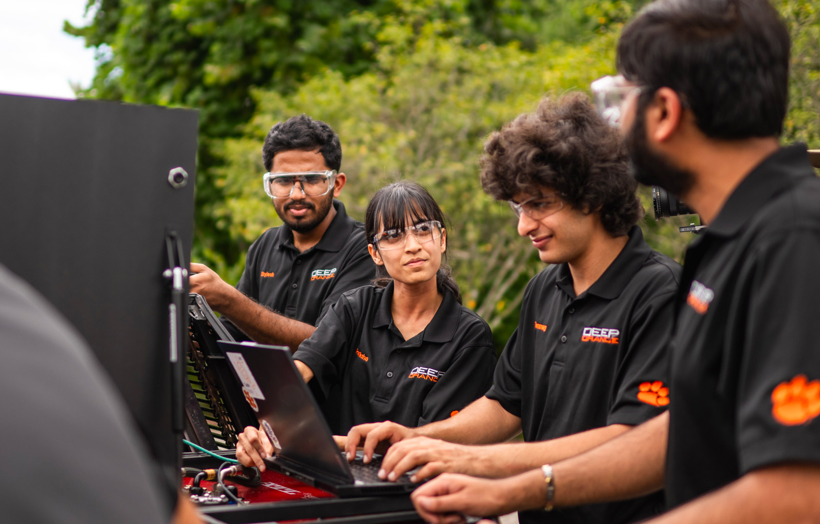 Students utilizing laptop while working on vehicle