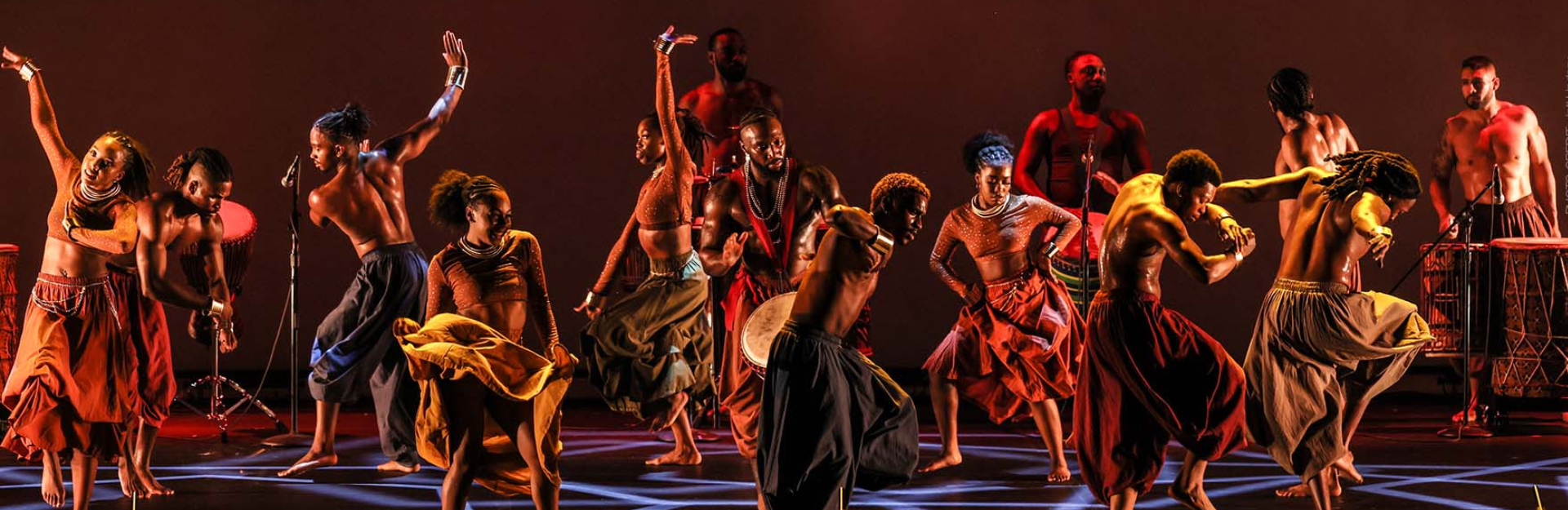 Production photo of Step Afrika. A large group of steppers dance and step in costume.