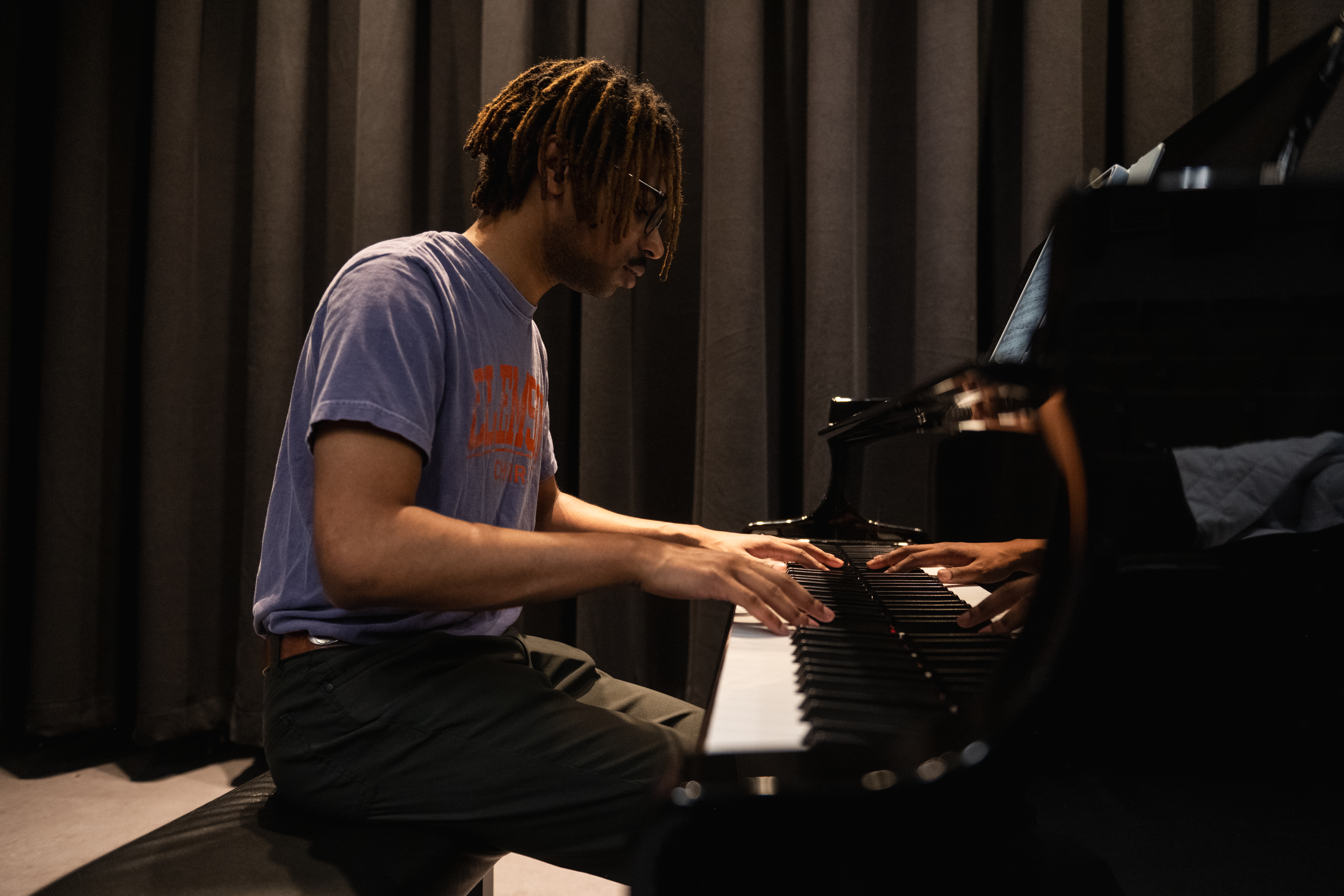 A student in a Clemson t-shirt practices on a baby grand piano in the Brooks Center recital hall.