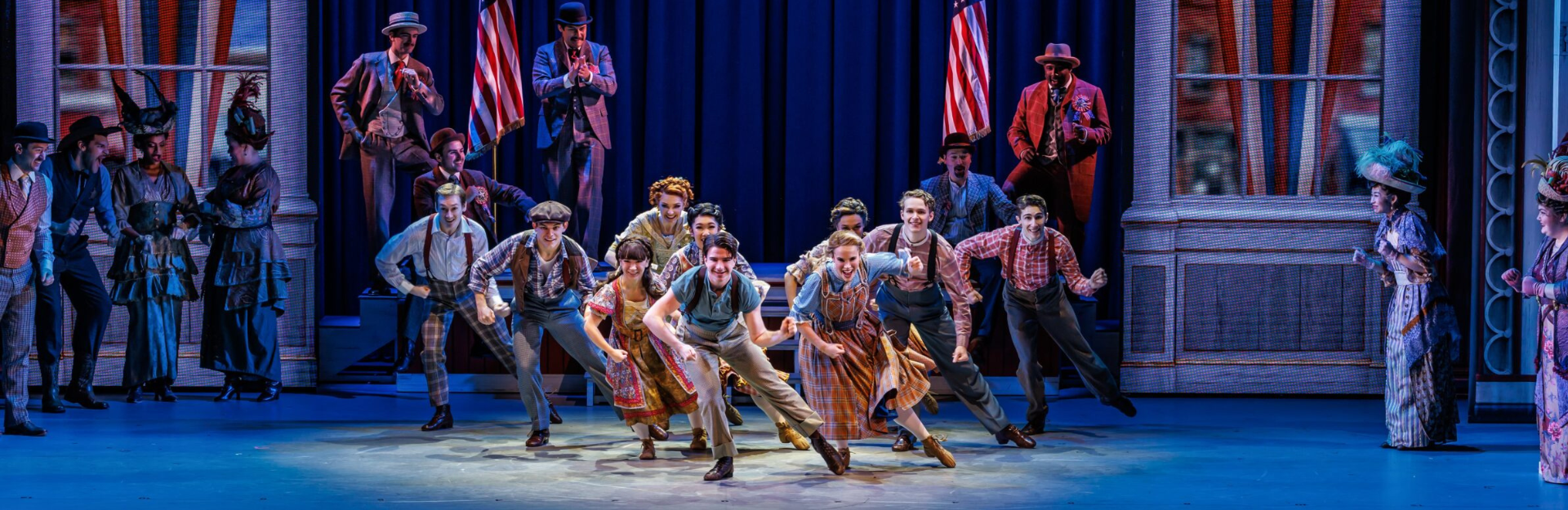 Production photo from The Music Man. A large ensemble dances on stage in period costumes.