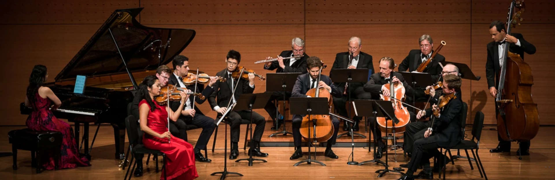 A large ensemble of musicians performs on stage in formal wear.