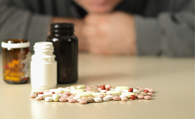 Pill bottles and pills on a table with an unknown man in the background.