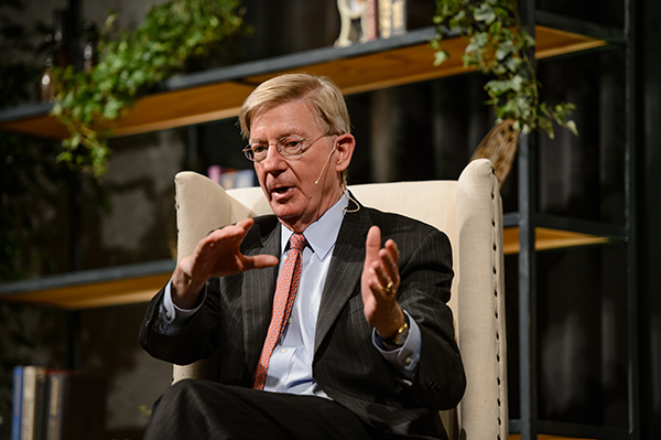 American political commentator George Will speaking in an interview setting, gesturing to emphasize his points.