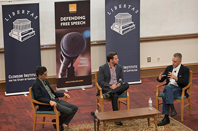Discussion panel featuring speakers seated on stage, discussing topics related to free speech, with Libertas and "Defending Free Speech" banners in the background.