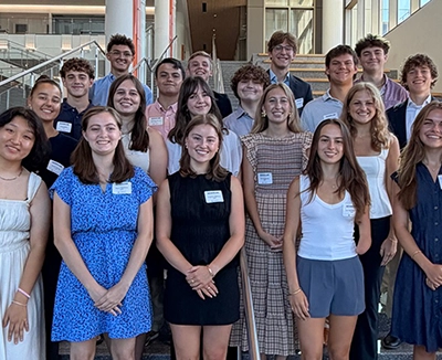 Group of smiling young adults wearing name tags, posing together indoors in a bright atrium.