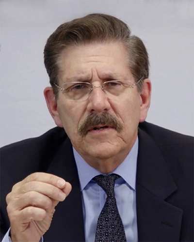 A man in a suit and tie, speaking directly to the camera, with an emphasis on communication.