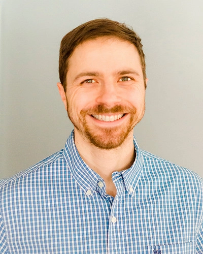 Smiling man in a blue checkered shirt against a gray background.