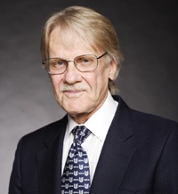 Professional portrait of an older gentleman in a dark suit and tie, featuring glasses and a confident expression.