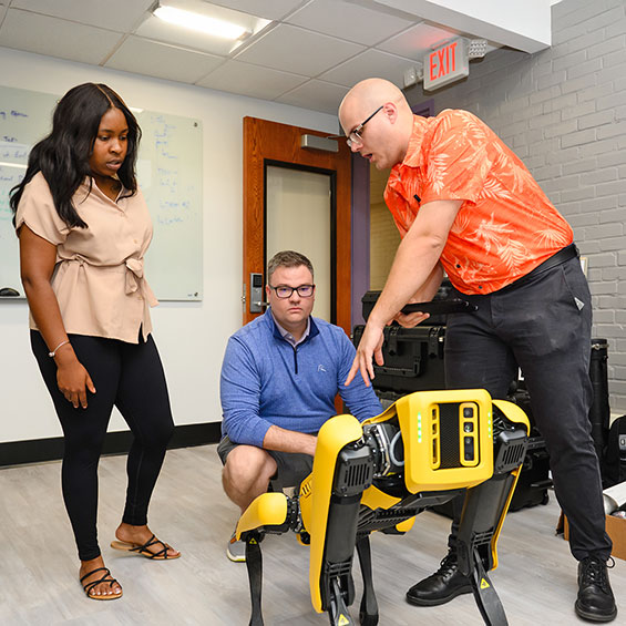 McNeese and Flathmann with student looking at Spot the robot