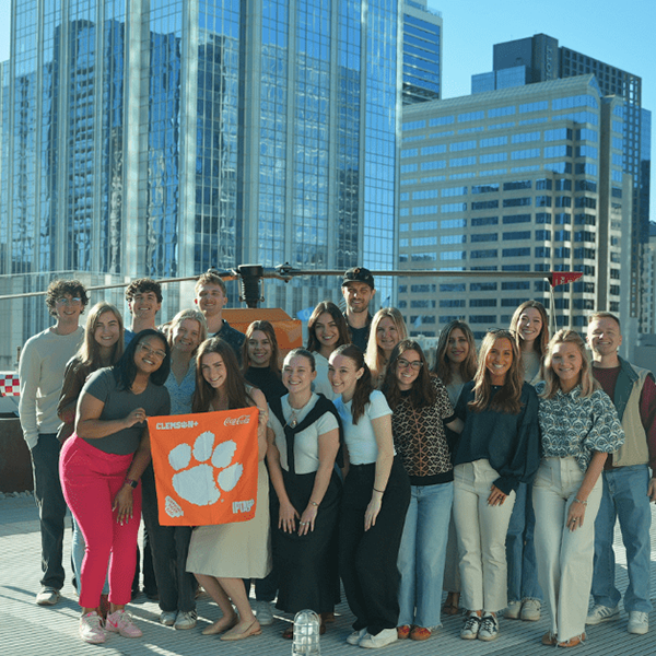 Group photo of students holding a Clemson University flag on a rooftop with a city skyline in the background.