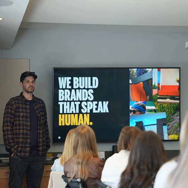 A man presenting in front of a screen displaying the text "WE BUILD BRANDS THAT SPEAK HUMAN."