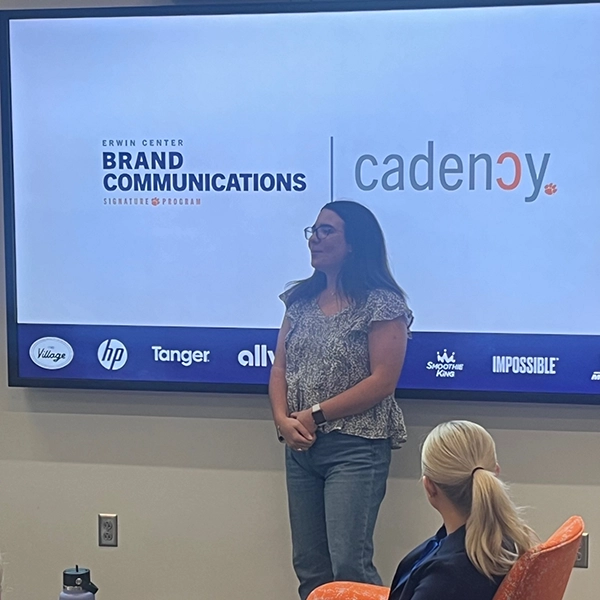 A presenter speaking in front of a screen displaying the logos for "Erwin Center Brand Communications" and "cadency."