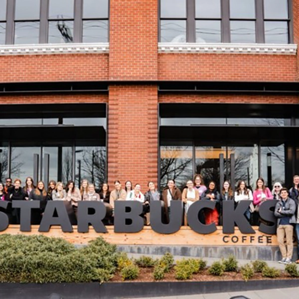 A group of people stands in front of a Starbucks store, featuring the iconic logo prominently displayed.