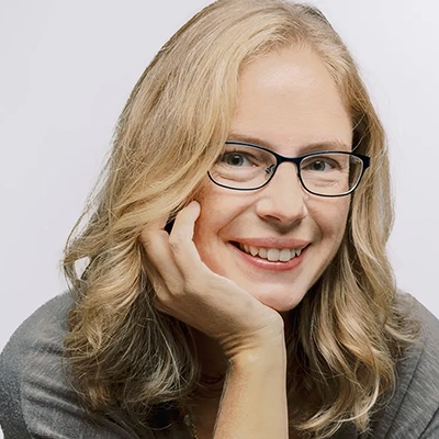 Professional portrait of a woman with glasses, smiling and resting her chin on her hand.