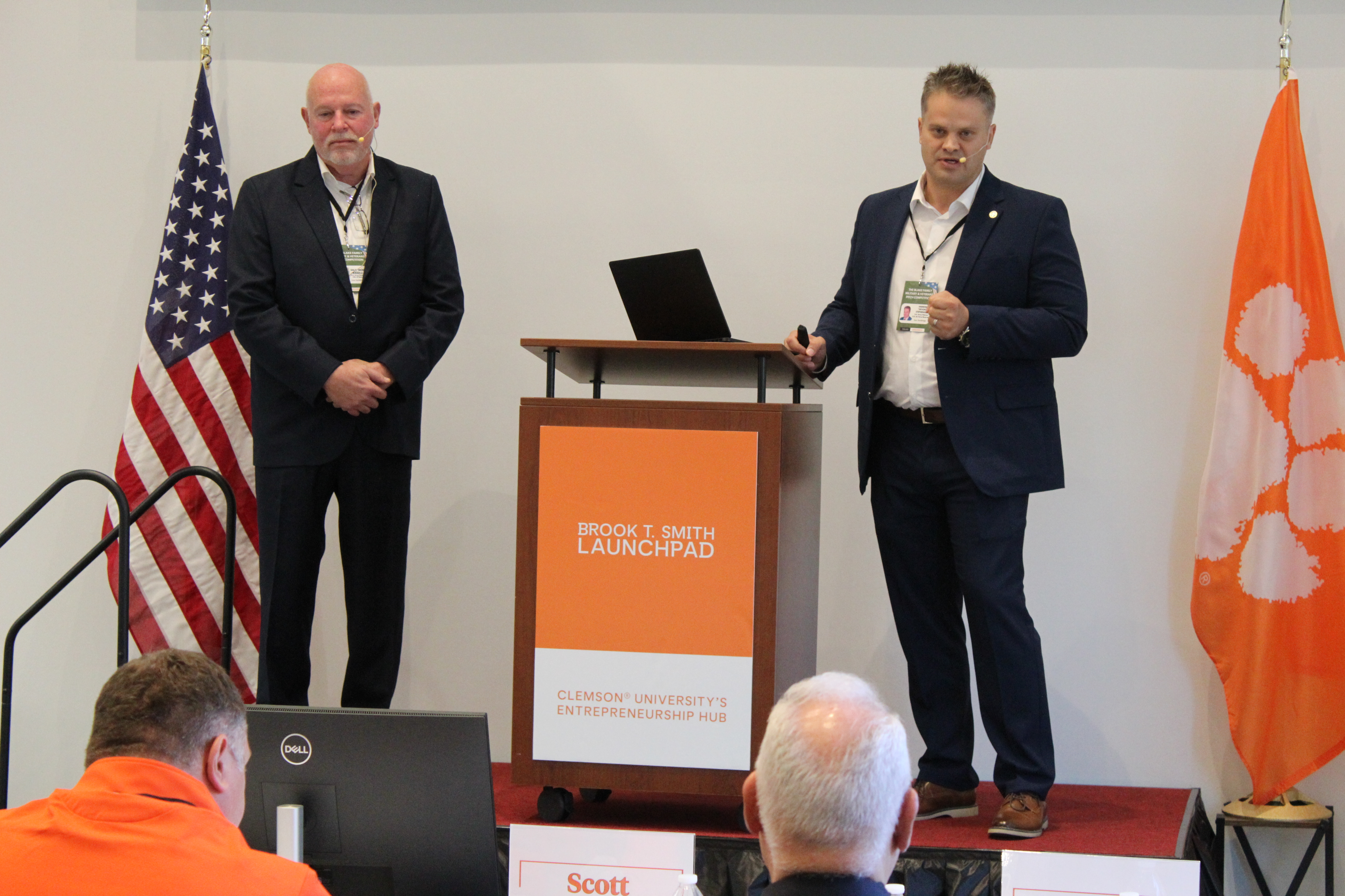 Two presenters on stage beside a podium with a laptop, speaking at the Brook T. Smith Launchpad at Clemson University.