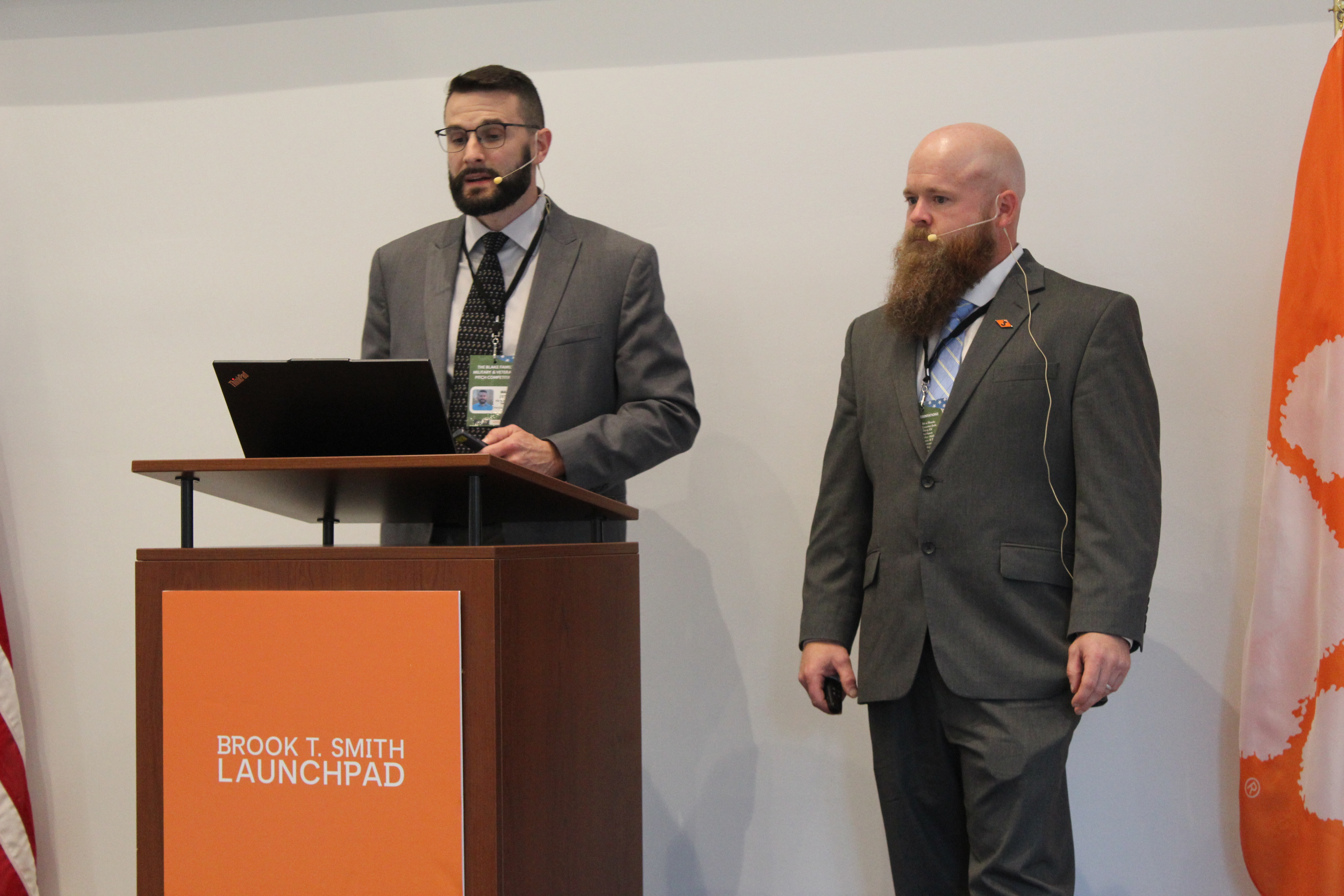 Two presenters in suits speaking at a podium with a laptop at the Brook T. Smith Launchpad.