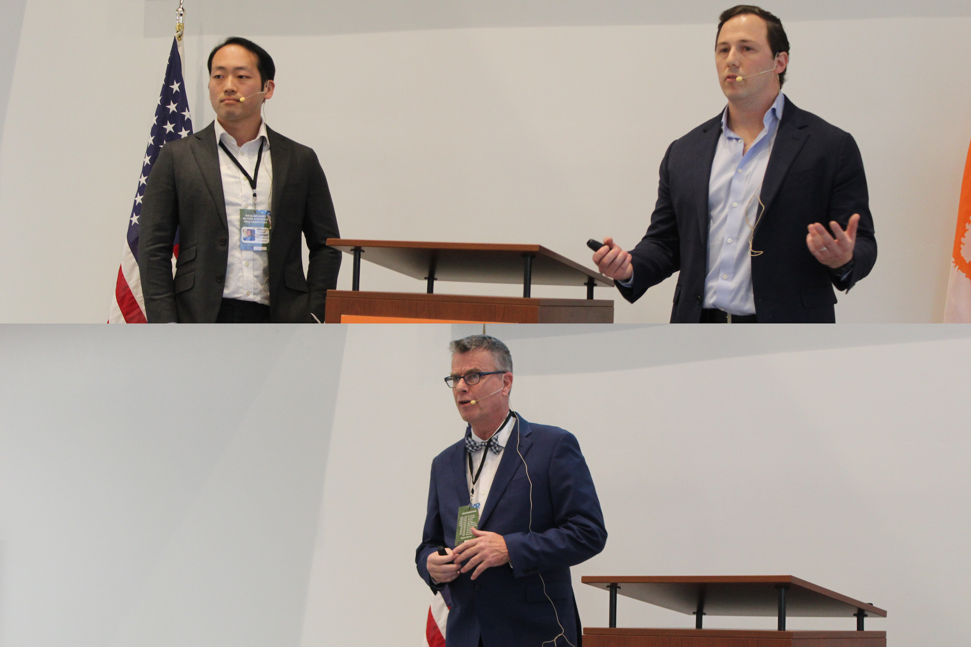 Two speakers presenting at a conference, with one speaker gesturing while the other listens. Flags are visible in the background.
