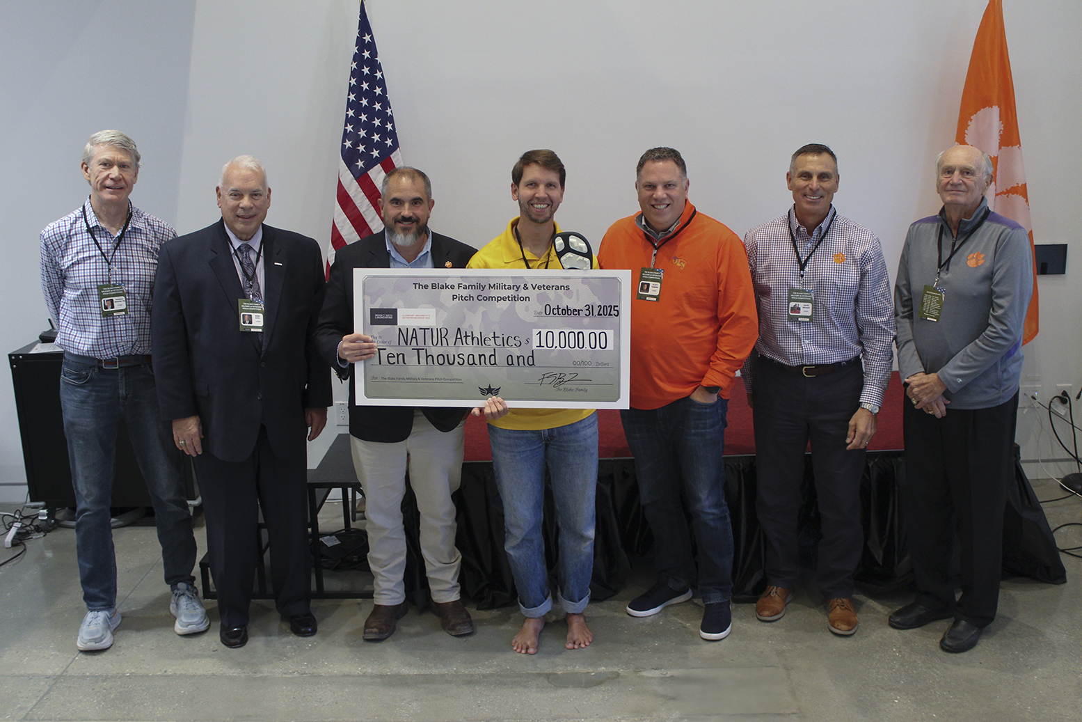 Group of men presenting a large check for $10,000 to support NATUR Athletics during a formal event.